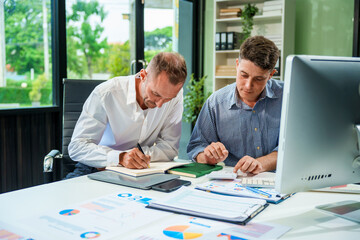 An Italian male and a Caucasian male sit at business desk in office meeting room, discussing...