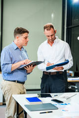 An Italian male and a Caucasian male sit at business desk in office meeting room, discussing...