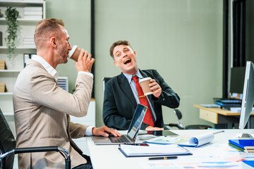 An Italian male and a Caucasian male, both in formal suits, sit at a business desk in an office...
