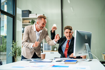 An Italian male and a Caucasian male, both in formal suits, sit at a business desk in an office...