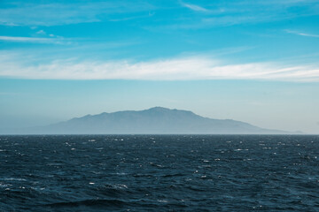 Oceanic Horizon. Serene view of the distant mountain range from California’s rugged coastline under a clear blue sky.