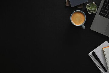 Top view laptop, cup of coffee and notebook on black background with copy space