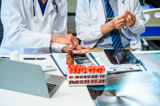 In a hospital meeting room,Italian male and Caucasian male discuss medical cases at desk with X-ray films, blood samples, patient information, on diagnosing heart disease and treatment guidelines.