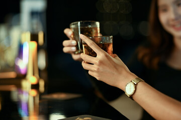 Two woman hands toasting with drinks at the modern bar. Nightlife, celebrations and friendship concept