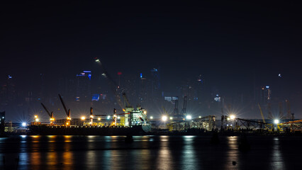 shipyard maintenance and repair container ship transport and oil ship reflection of water in front, business and industry concept at night over lighting and city light buildings