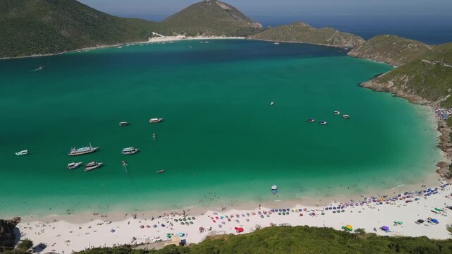 Stunning drone aerial view of Arraial do Cabo, Cabo Frio, Brazil with a white sand beach with crystal blue ocean waters and majestic island mountains in the background.
