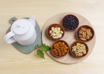 Top angle view of dried nuts like walnut, pecan, cashew nuts, almond and blueberries on wood dish with white kettle, South Korea
