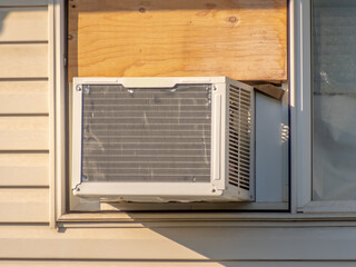 A close-up of a window with an air conditioner installed in the lower portion and a wooden board...