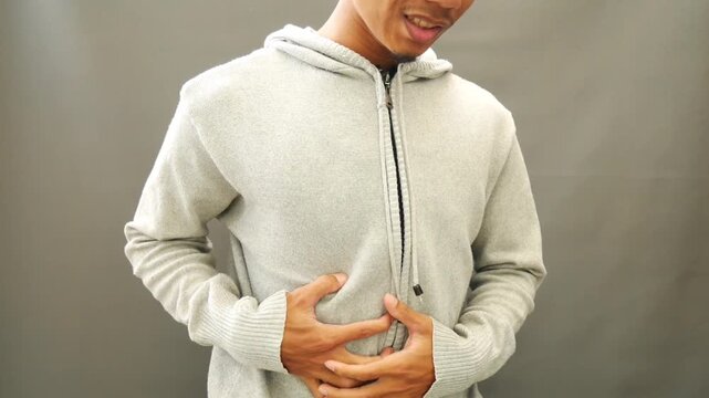 The young man wearing a gray sweater grimaced while holding his aching stomach