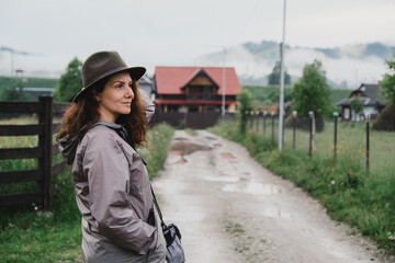 Fototapeta premium Young woman standing near house in mountain village in summer. Summer trip on mountain routes in Europe.