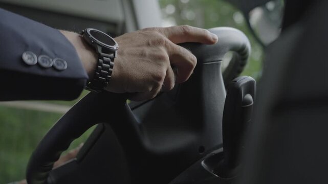 Professional bus driver, operating and driving the bus on road. Close shot of man's hand controlling the steering of the passenger vehicle.