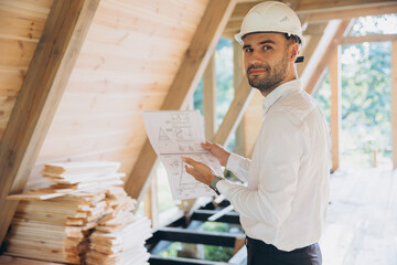 Architect wooden buildings. Man stands under frame wooden house. Man architect studies...