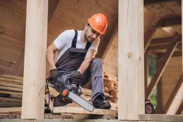 Man worker in work uniform and gloves working with chainsaw of woodcutter sawing chain saw in...