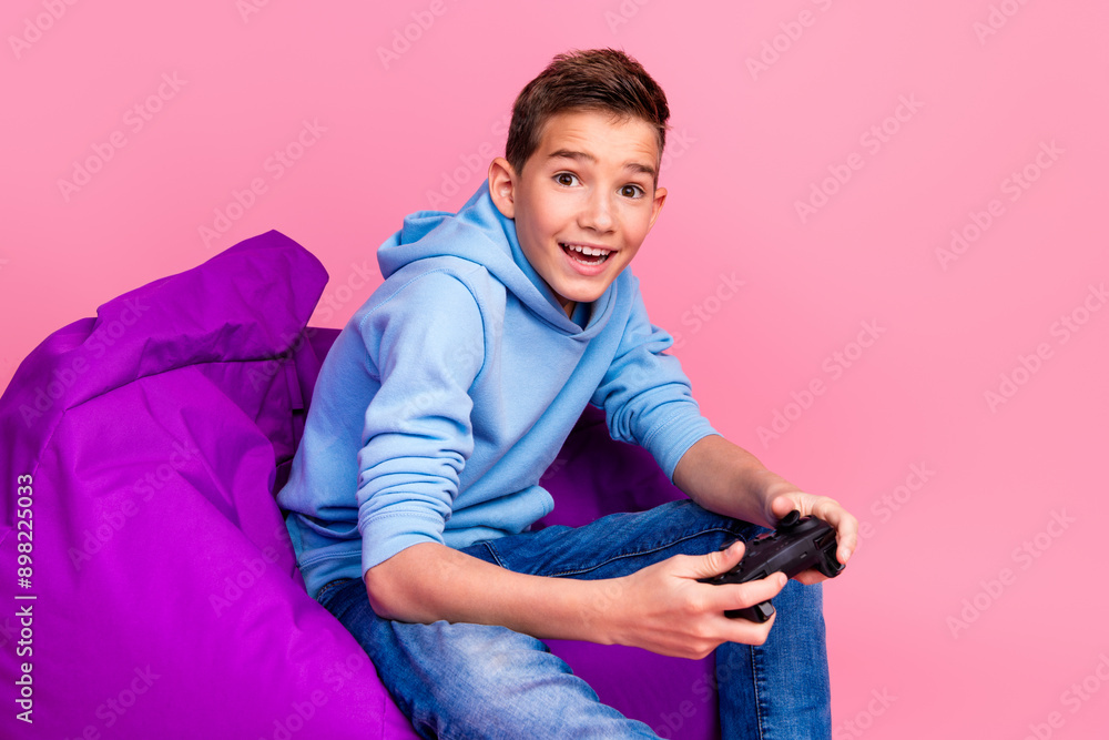 Wall mural photo portrait of cute teen boy beanbag hold joystick play videogame dressed stylish blue clothes is