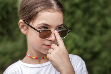 Little girl holds sunglasses with her finger and looks into the distance