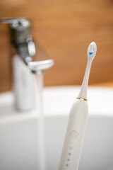 Upright electric toothbrush on sink edge, faucet background.