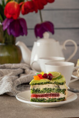 A colorful layered cake slice with green frosting, red berries, and yellow citrus slices on a white plate