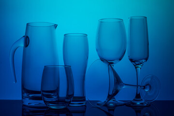 Glassware collection on a blue background, including a pitcher, tumblers, and stemmed glasses