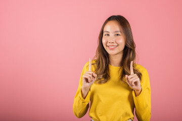 Asian happy portrait beautiful young woman standing makes gesture two fingers point upwards above presenting product something, studio shot isolated on pink background with copy space, point up