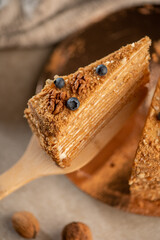 One slices of layered honey cake topped with blueberries and nuts, placed on a wooden spatula and plate