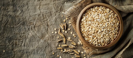 Fototapeta premium Top down view of oat groats or spikes in a wooden plate on a rustic tablecloth with space for text or images amid selective focus. Creative banner. Copyspace image
