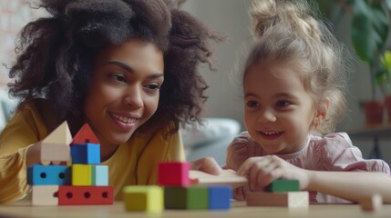 A cute little girl sits at a table with her mother, playing with colorful wooden bricks to build a pyramid.
