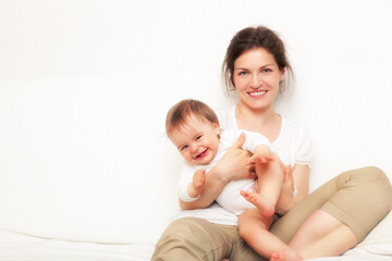 Happy mother playing with baby on white sofa