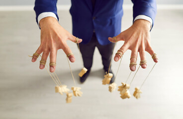 Top view of businessman wearing suit controlling wooden human figures marionettes by hands hanging...