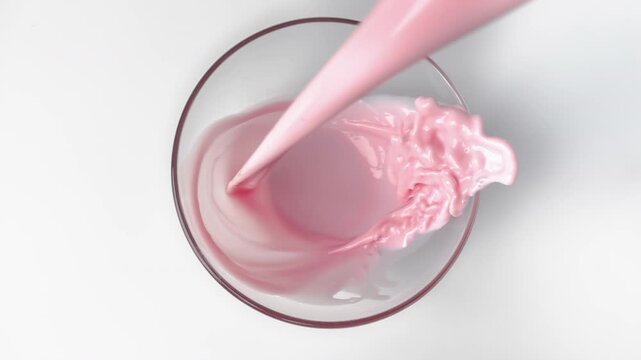 Strawberry smoothie with cream pouring slowly into glass in white background, top view in kitchen