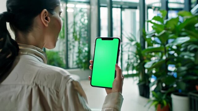Young woman holding showing phone with chroma key green screen over blurred indoor cafe background