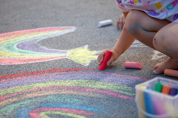 Kid hand draws a rainbow with multi-colored chalk on the asphalt. Drawing multicolored chalk stick,...