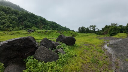  serene landscape featuring rocks on a meadow under a cloudy sky, with the Sahyadri hills in...
