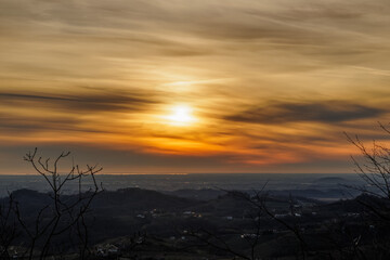 vista dettagliata dall'alto da alcune colline del sole che tramonta all'orizzonte dietro vari strati di nuvole e colora il cielo di sfumature di arancione e giallo