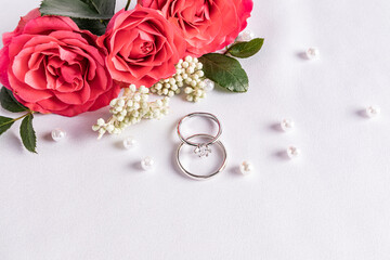 Delicate wedding arrangement with two wedding platinum rings on a white satin background with pearl beads and flowers. postcard. invitation. cover
