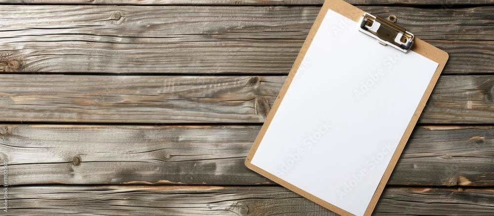 Poster top view of a clipboard with white paper on a wooden backdrop suitable for use as a mock up copy spa