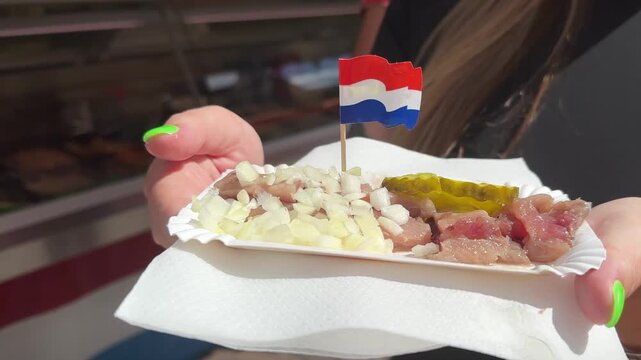 Holding herring with pickles, onions and Dutch flag. Eating traditional street food in the Netherlands.