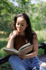 Obraz premium Portrait of asian woman reading blurred book on bench in park