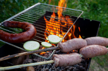 Grilled sausages on grill with smoke and flame on a meadow. Barbecue picnic