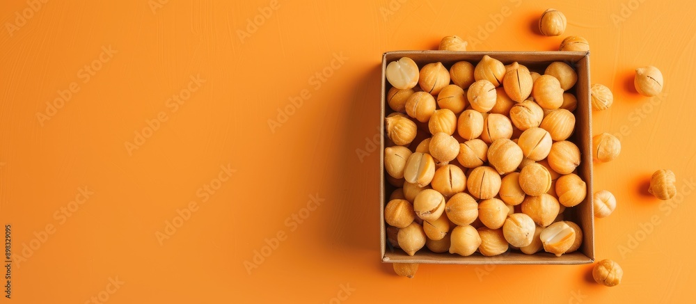 Poster A box of natural macadamia nuts on an orange background captured from above with ample copy space image
