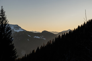 luce calda del sole al tramonto che illumina le valli e le sagome delle catene montuose, parzialmente in controluce, in inverno