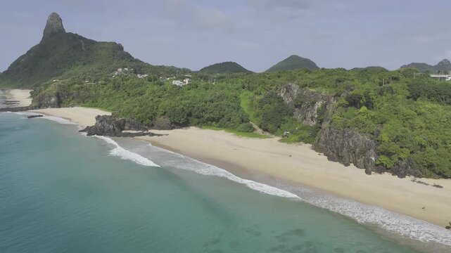 Drone flies along Praia Bode toward Praia do Americano and Praia do Boldr&oacute; with Morro do Pico in background on sunny afternoon in Fernando de Noronha, Pernambuco, Brazil