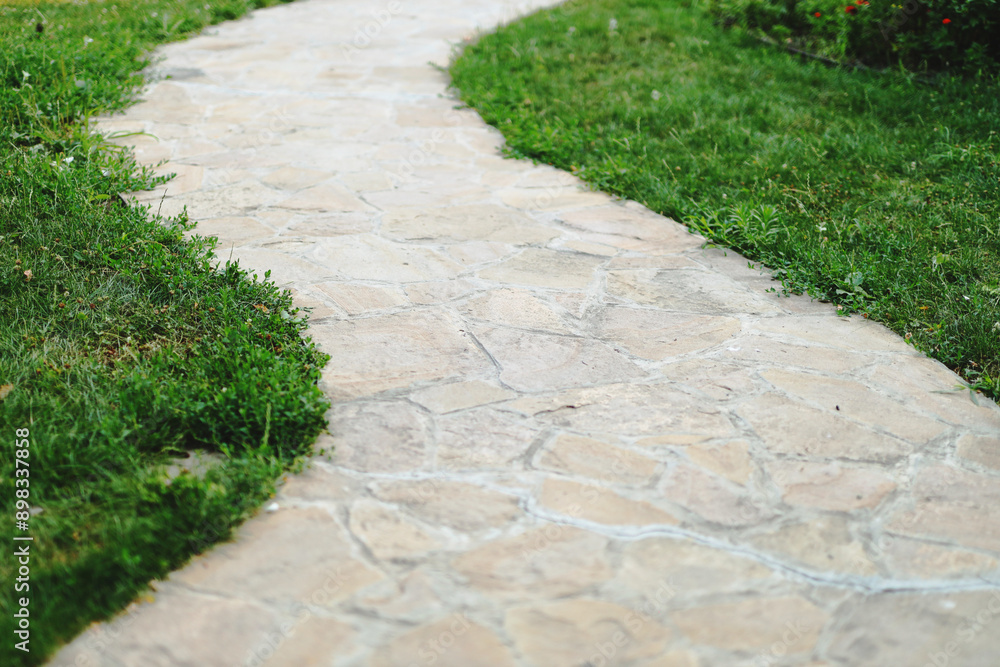 Poster a stone walkway with grass on either side. the walkway is narrow and has a slight curve