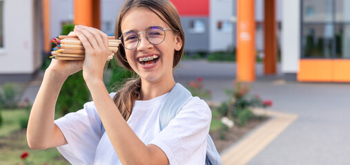Obraz premium Schoolgirl with pencils in hands close-up. Student with school supplies on school background. Smiles