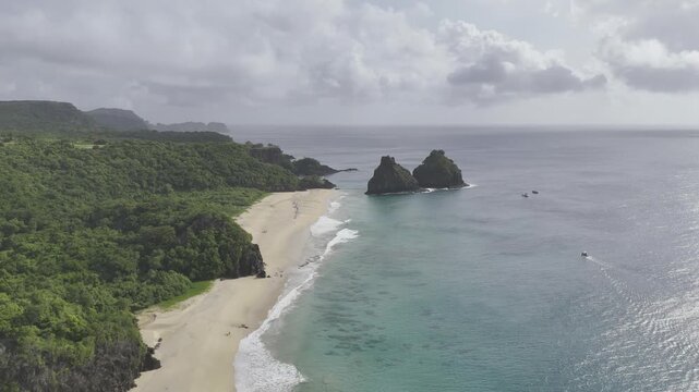 Drone flies backwards high over Praia do Boldr&oacute;, facing Praias do Americano, do Bode, da Cacimba do Padre and Morro Dois Irm&atilde; on partially cloudy afternoon in Fernando de Noronha, Pernambuco, Brazil