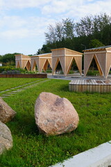 Four modern wooden arbors, gazebos. Landscape design with green grass. Brown stones in the front....