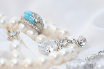 Close-up of elegant jewelry pieces, including pearls, silver rings, and a blue gemstone ring on a white fabric background. This image captures the luxury and sophistication of fine jewelry