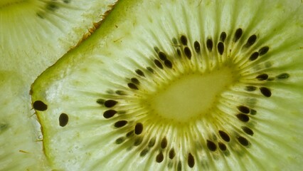 Macro shot of fresh juicy green kiwi slice against skylight, showing flesh and seeds with watery...