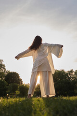A person in flowing white garments extends their arms in a wide gesture against a sunset backdrop. The photo highlights the sense of liberation and harmony with the natural world.