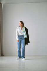woman displays effortless style in a white blouse, blue jeans, and white sneakers, with a black...