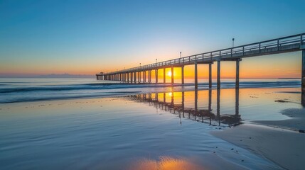 Sunset over a wooden pier on a sandy beach.